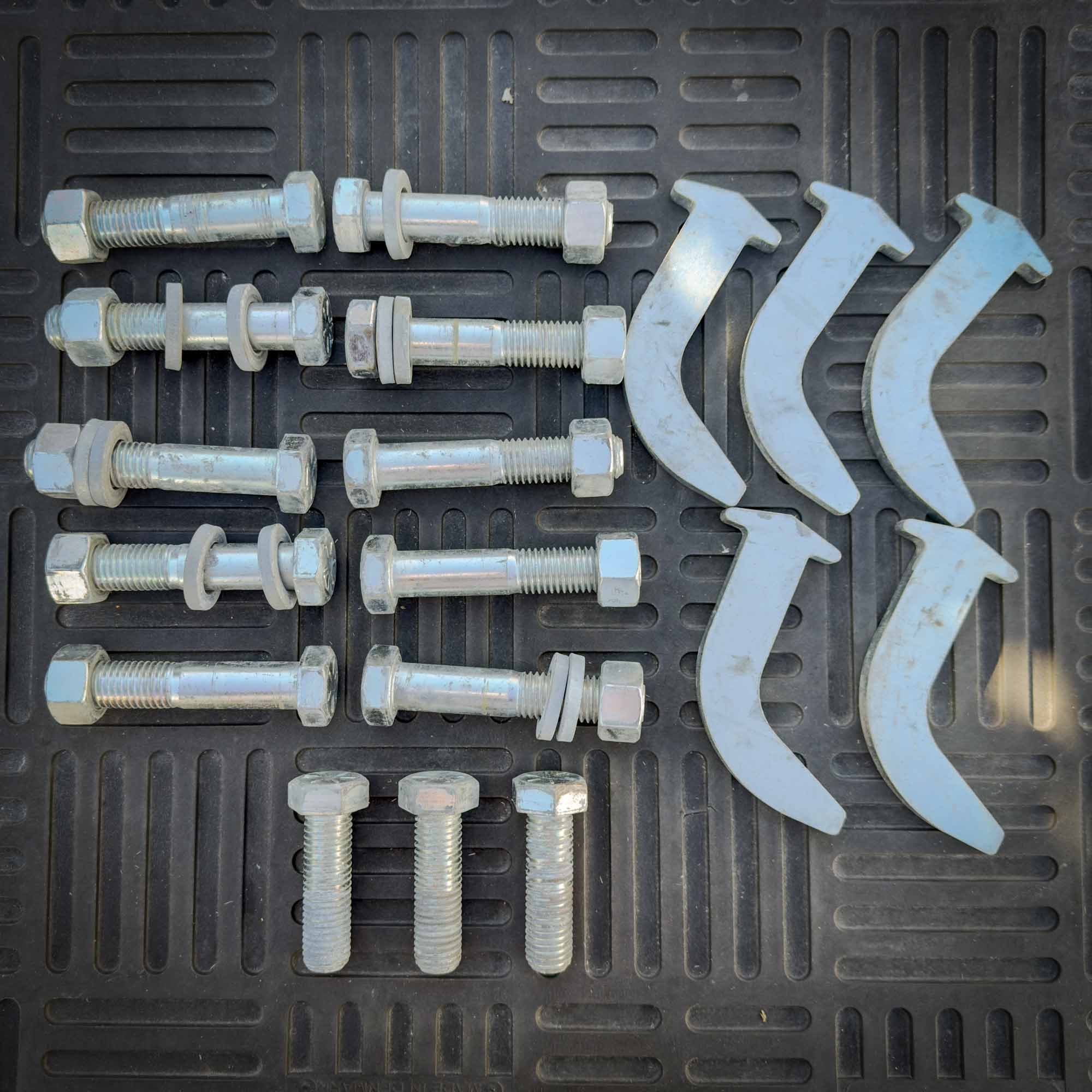 A set of bolts, washers, and curved metal components laid out for assembly of the Front Mount Scarifier for John Deere Motor Graders from Obtainium Science and Surplus.