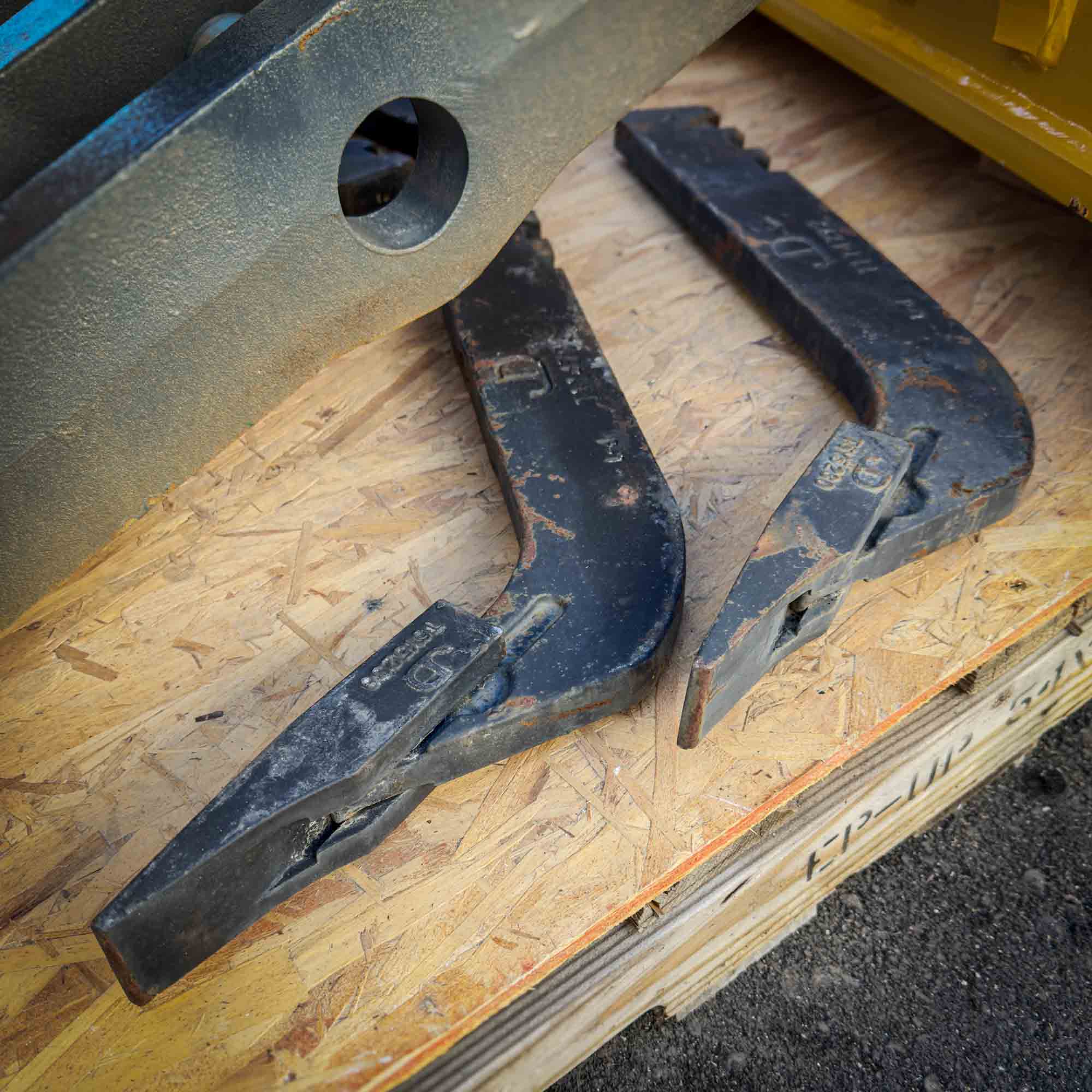 Two scarifier shank and tooth assemblies for the Front Mount Scarifier for John Deere Motor Graders from Obtainium Science and Surplus, lying on a wooden pallet.