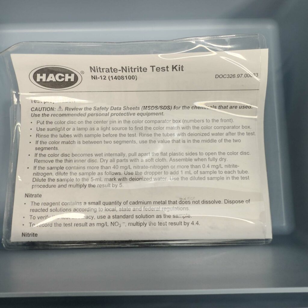 A sealed plastic bag inside the Hach Water Test Kit for Nitrites and Nitrates from Obtainium Science and Surplus, containing an instruction sheet labeled "Nitrate-Nitrite Test Kit" from Hach. The text provides details on the test procedure and safety precautions.