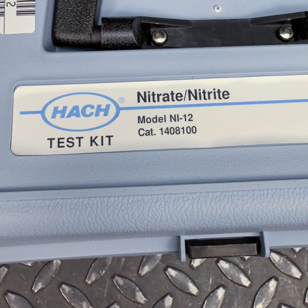 Close-up of the label on the blue carrying case of the Hach Water Test Kit for Nitrites and Nitrates from Obtainium Science and Surplus. The label reads "Hach Nitrate/Nitrite Test Kit, Model NI-12, Cat. 1468100," with the Hach company logo above the text.